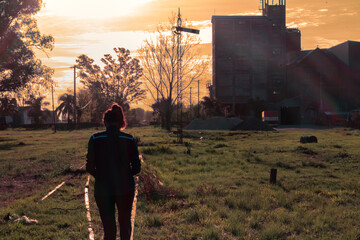 Panoramic view of an adult woman walking on railroad tracks in a rural town with an scenic sunset sky as background