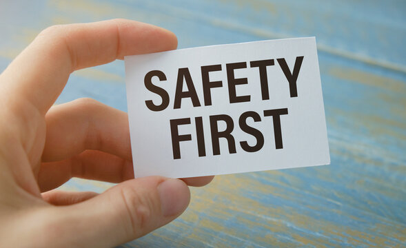 Safety First In Unsafe Workplace Concept Photo. Hand Of Staff Is Holding The Text Sign With Blurred Background Of Drilling Rig Or Refinery Plant Equipment At Worksite Location.