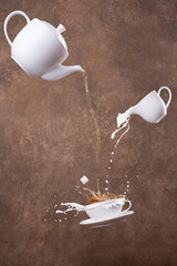 flying cups in pouring hot tea from teapot on a brown background. Levitation.