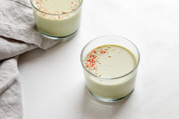 Matcha panna cotta desserts with confectionery decor in a glass on a white background and a grey napkin next to it.