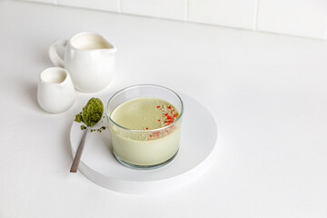 Matcha panna cotta desserts with confectionery decor in a glass on a white background and two milk...
