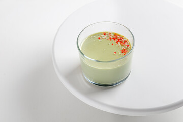 Matcha panna cotta dessert with confectionery decor in a glass on a white cake pan and white background.