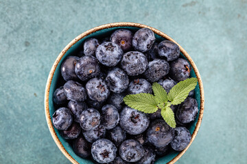 Ripe blueberries with water drops in a bowl on a pastel background,