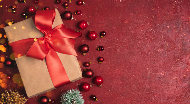 Christmas gift box with red ribbon and red christmas balls on the red stone background