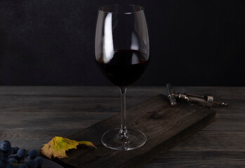 Composition with a glass of red wine and grapes on a dark background of gray wooden boards. Winemaking concept. Still life with wine in a dark key