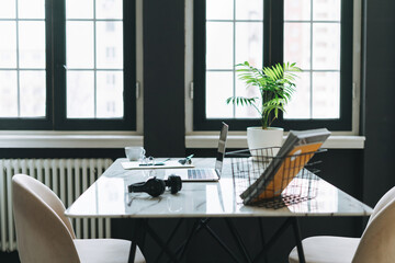 Working place with cup of coffee, notes, open laptop, eye glasses and smartphone on white marble table in the dark modern office room, business interior