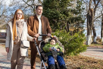 Fototapeta premium A young family, with a child, in a stroller, walking in the park