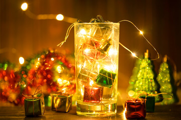 Warm lights in a glass with Christmas gift boxes on bokeh blur background.