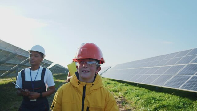 Scientific tour. Solar station. Cute boy teenager in helmet walking on industrial solar photovoltaic construction. Sustainable development. Solar farm.