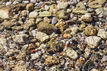 Background from stones and flowing waves on the sea beach. Summer holidays and coastal nature concept