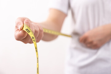 A woman in a white t-shirt holds a yellow centimeter tape in her hands.