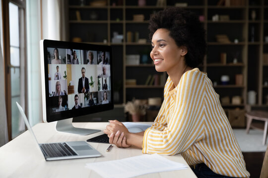 Happy African American remote employee talking on video conference call to colleagues, sitting at computer monitor, speaking to audience, attending virtual business meeting, negotiations, seminar