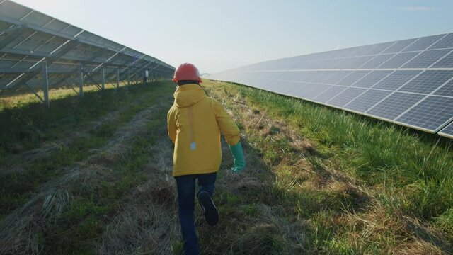 Running young teenager boy wearing protective helmet and gloves visiting professional modern huge outdoor power station. Solar panels. Solar plant.