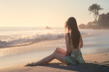 Attractive young woman sitting on the beach looking at the ocean, Malibu, Los Angeles, California