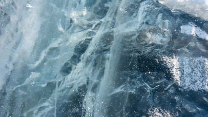 Turquoise ice of the frozen Lake Baikal. Close-up. Full screen. Deep cracks and some snow on the surface are visible.