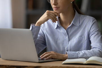 Cropped close up view serious thoughtful businesswoman in glasses sit at desk looks at laptop read e-mail, thinks over telework task, e-learning use modern tech, internet connection Technology concept