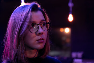 Cute young woman in a dark room with colored lights wearing glasses.