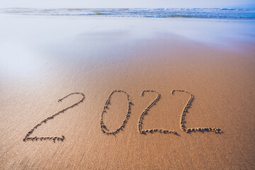 2022 hand written sign on sandy beach. Abstract seascape in golden and blue colors. Happy New Year 2022 concept