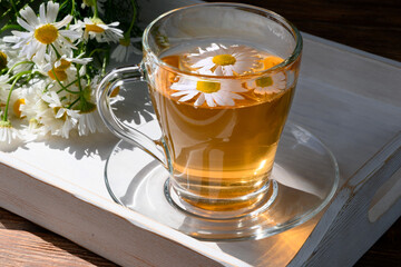 Healthy herbal tea in teacup with chamomile flowers on white wooden tray