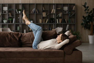 Peaceful young woman lying on comfy soft sofa with legs raised feels carefree spend lazy weekend...