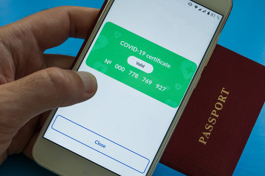 The man's hand holds a passport and a smartphone with a valid covid-19 digital vaccination certificate on the screen. Close-up. Blue background.