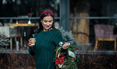 Young woman with a Christmas wreath and a cup of coffee on a city walk.