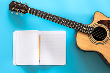 Acoustic guitar and notepad on a blue background, top view.
