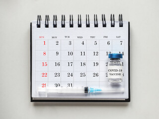 Syringes, injection vials and a calendar page lying on the table. Close-up, indoors, top view. Day light, studio photo. Healthcare concept