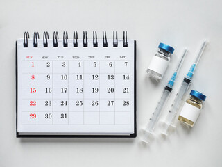 Syringes, injection vials and a calendar page lying on the table. Close-up, indoors, top view. Day light, studio photo. Healthcare concept