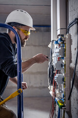 A male electrician works in a switchboard with an electrical connecting cable.