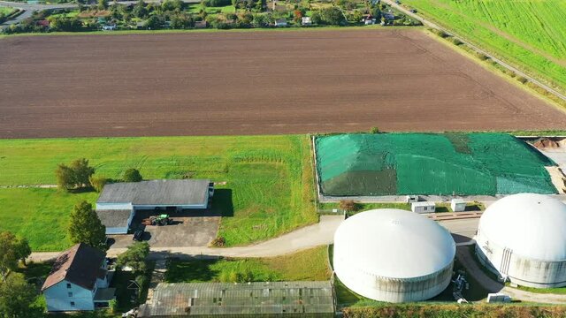 Aerial view of small white biogas plant with white digesters next to farm behind cropland