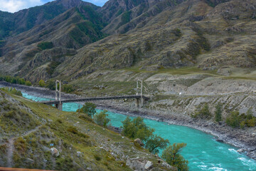 an old double-chain bridge with pylons across the river in a mountain valley in autumn. fuzzy focus