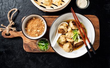 Sesame Chicken Dumplings in Spicy Broth with Garlic Crisps. Black background. top view