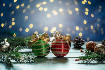 Green and red Christmas bulbs with golden bows, fir tree branches and ornaments on wooden background with Christmas lights bokeh