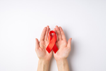 First person top view photo of woman's hands holding red satin ribbon in palms symbol of aids awareness on isolated white background with blank space