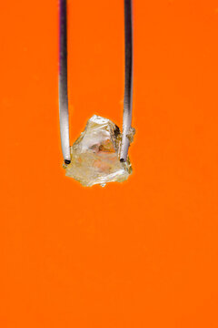 THCA Live Resin Diamonds Cannabis Concentrate between tweezers on an orange background. 