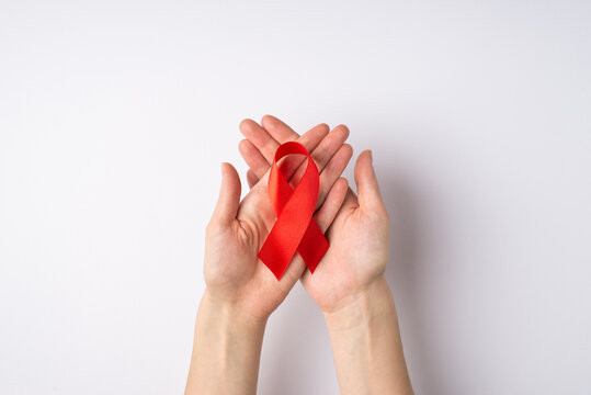 First person top view photo of female hands holding red silk ribbon in crossed palms symbol of aids awareness on isolated white background