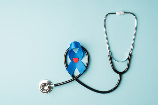 Top view photo of stethoscope and blue silk ribbon with small red heart symbol of prostate cancer awareness on isolated pastel blue background with blank space