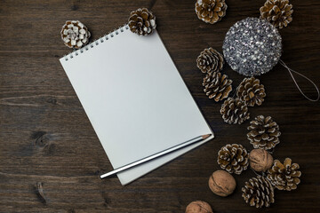 On the wooden table are a notebook, decorated with pine cones, a Christmas ball and a pencil