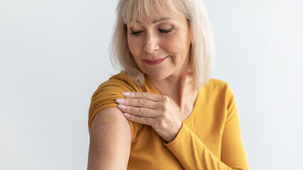 Vaccinated Senior Female Looking At Arm With Plaster, Gray Background