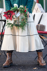 Christmas wreath in the hands of a stylish woman, city walk.