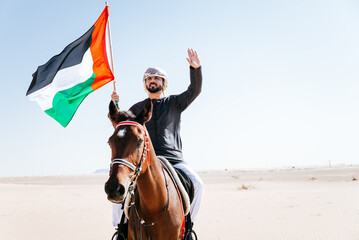 Young adult with Kandura, the emirates traditional clothes, riding his horse in the desert