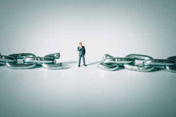 Macro photo of thoughtful businessman figurine standing between broken chain. Pondering miniature...
