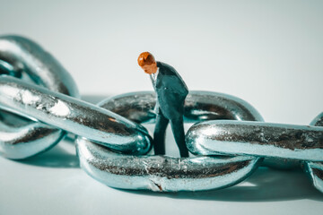 Macro photo of thoughtful businessman figurine standing in a ring of chain. Business failure,...