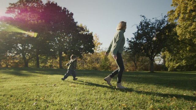 A woman has fun with her baby, running together on the grass in the rays of the sun