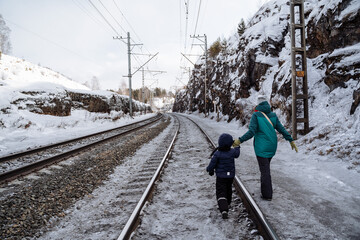 A child holds his mother by the ruga walking on the railway in the winter. Walk along the railway