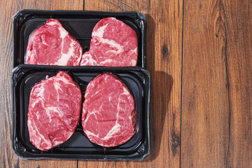 Rib eye steaks on a black plastic tray on a wooden table. Premium beef product. Fresh meat. Butcher craft. Food supply industry.