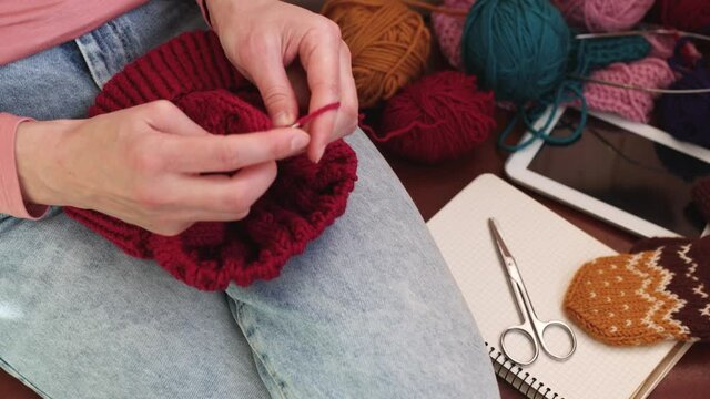 A woman knits a hat from woolen yarn. Self made. Colored yarns and knitting needles.