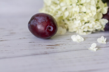 Ripe plums on a wooden background, hydrangea flowers lie nearby.