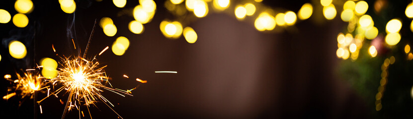 Christmas or New Year party sparkler with blurred gold lights on dark background. Festive Magic...